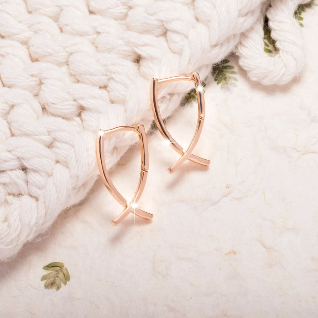 Rose gold coloured cross-shaped earrings on a plain background.