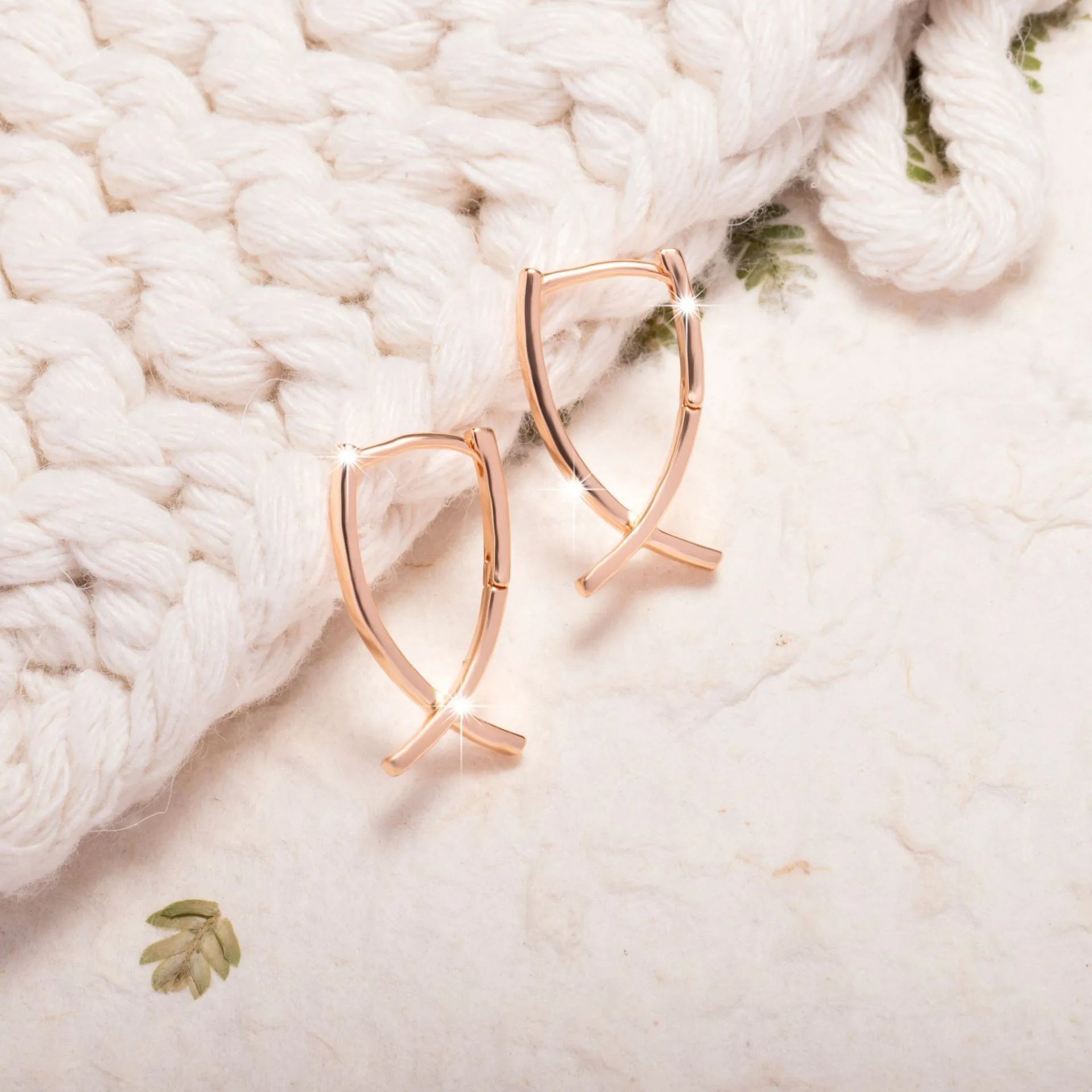 Rose gold coloured cross-shaped earrings on a plain background.