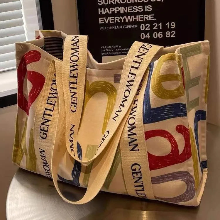 Large canvas tote shoulder bag with printed design in black letter, coloured letter, and pattern styles.