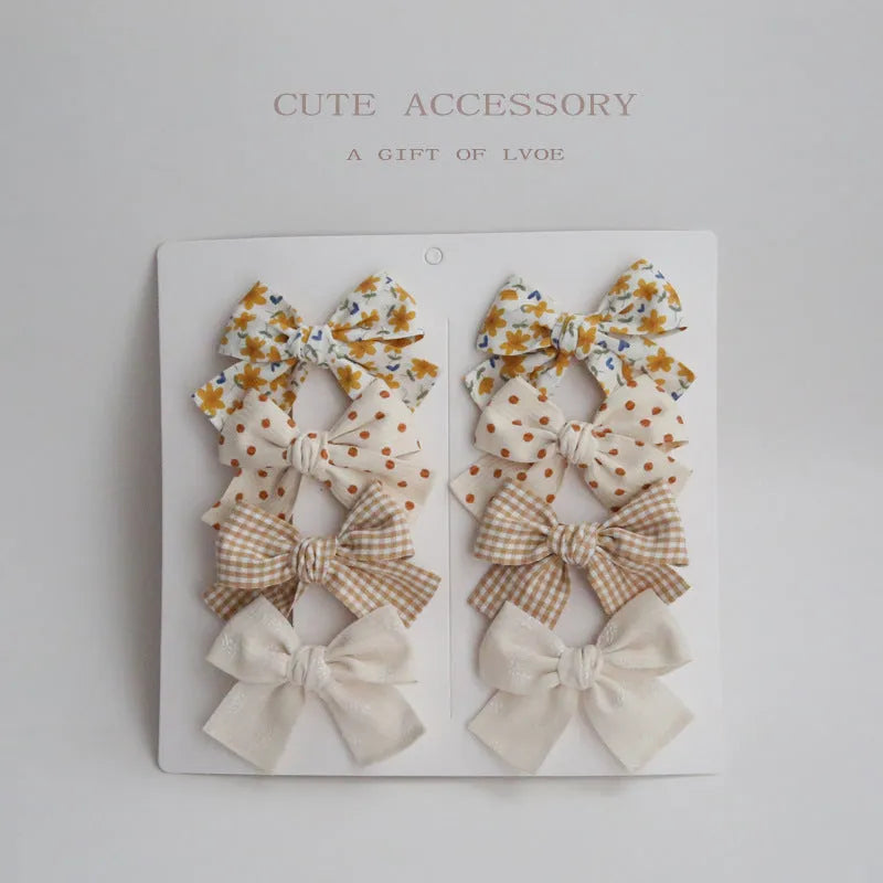 Set of eight cloth hairclips for children with dovetail bow designs in various colour patterns.