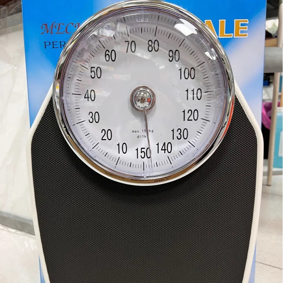 Black mechanical bathroom scale with large analogue dial showing weight pointer, placed on a floor.