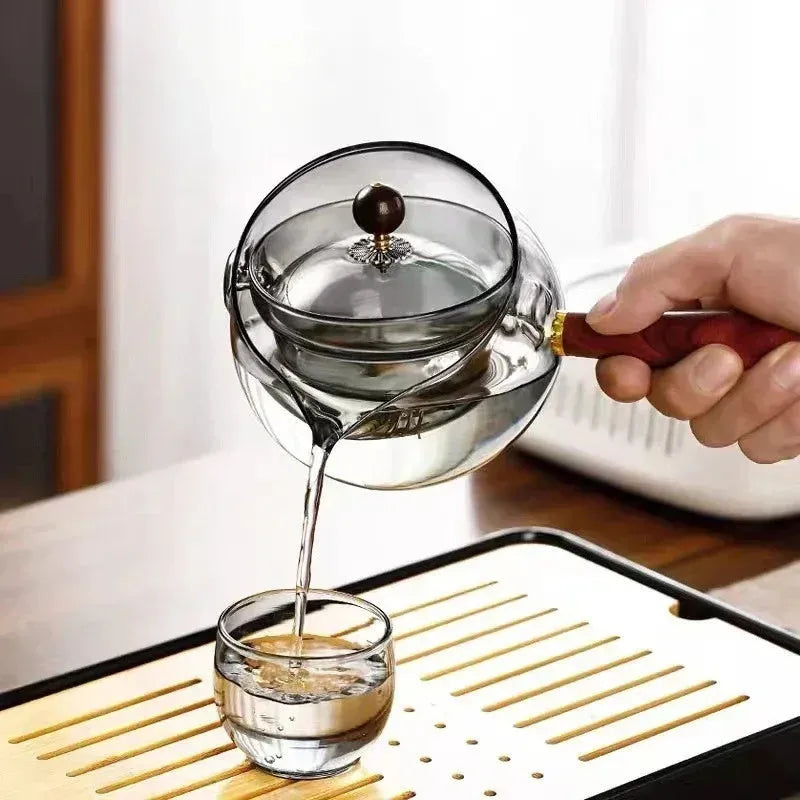 Semi-automatic rotary heat-resistant glass teapot with infuser and wooden handle on a table, transparent or grey