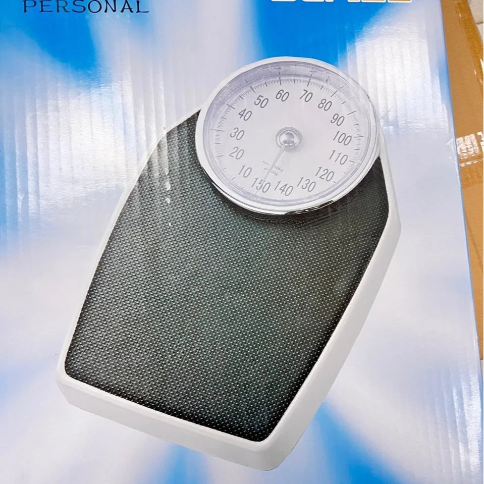 Black mechanical bathroom scale with large analogue dial showing weight pointer, placed on a floor.