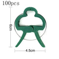 Green plastic plant fixing clips holding climbing plant stems against a support structure