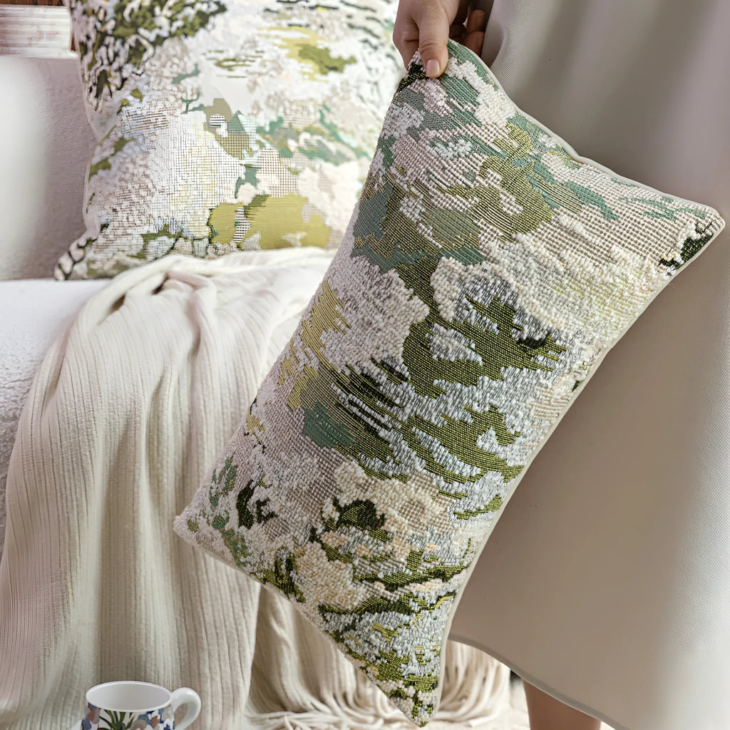 Green square pillow with abstract botanical plant and flower pattern on a sofa.