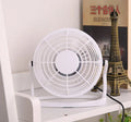 Mini black USB desk fan on a table next to a laptop, showing adjustable tilt angle.