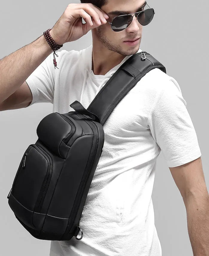 Black PVC outdoor shoulder bag with a square shape, showing the air cushion strap and front pocket.
