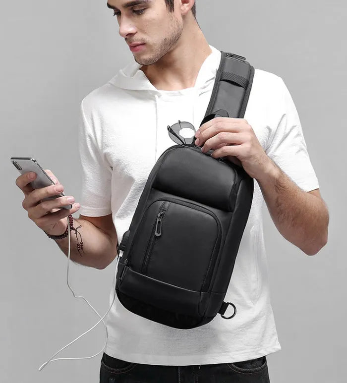 Black PVC outdoor shoulder bag with a square shape, showing the air cushion strap and front pocket.