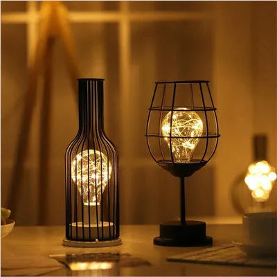 Minimalist hollow wrought iron table lamp in red wine bottle style on a wooden desk.