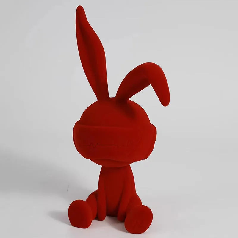 Suede blindfold rabbit resin ornament in green, blue, or red colours on a shelf.