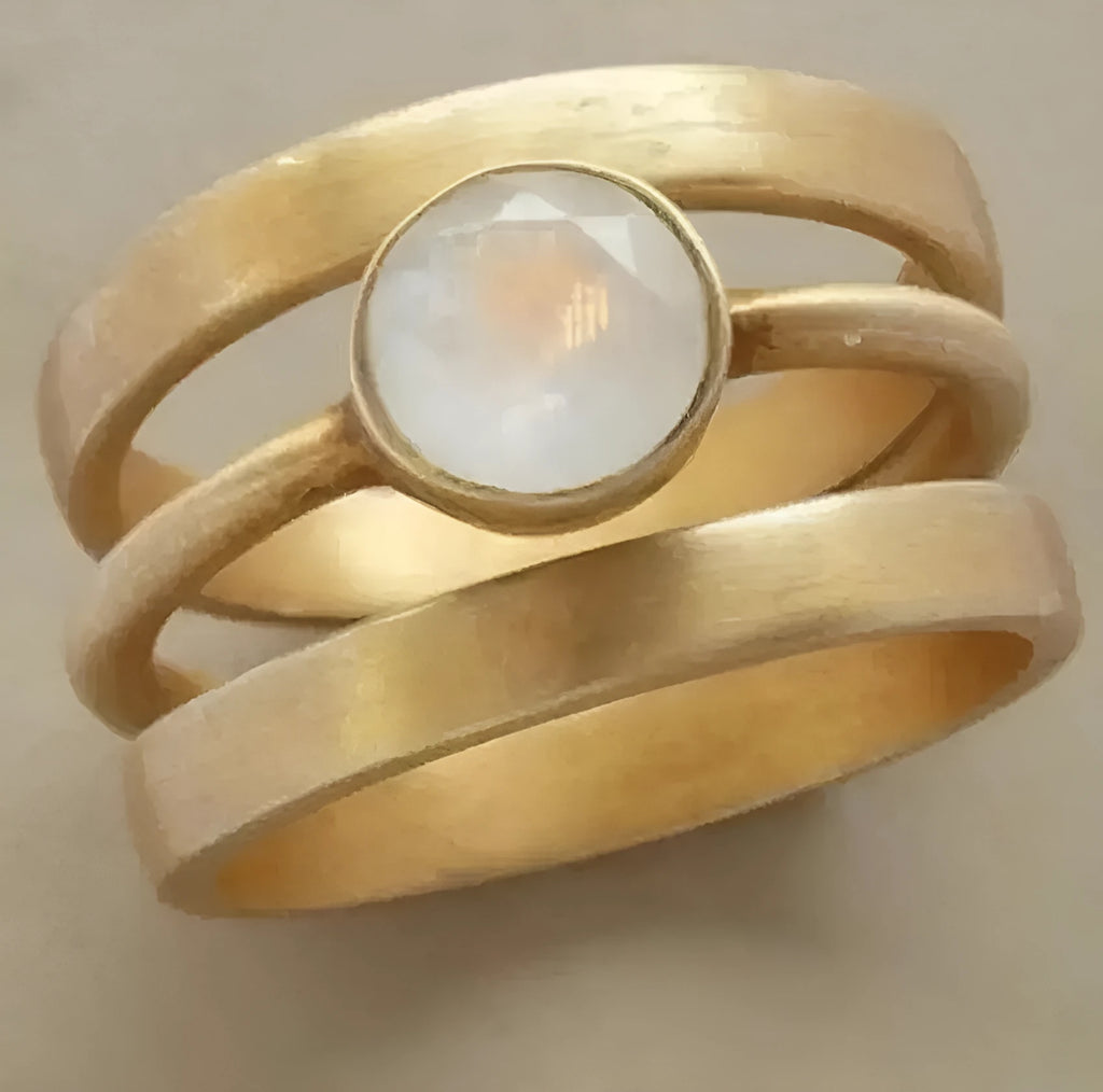 Gold geometric ring with linear detail and a small white chalcedony stone inlaid on a titanium steel band.