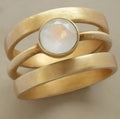 Gold geometric ring with linear detail and a small white chalcedony stone inlaid on a titanium steel band.