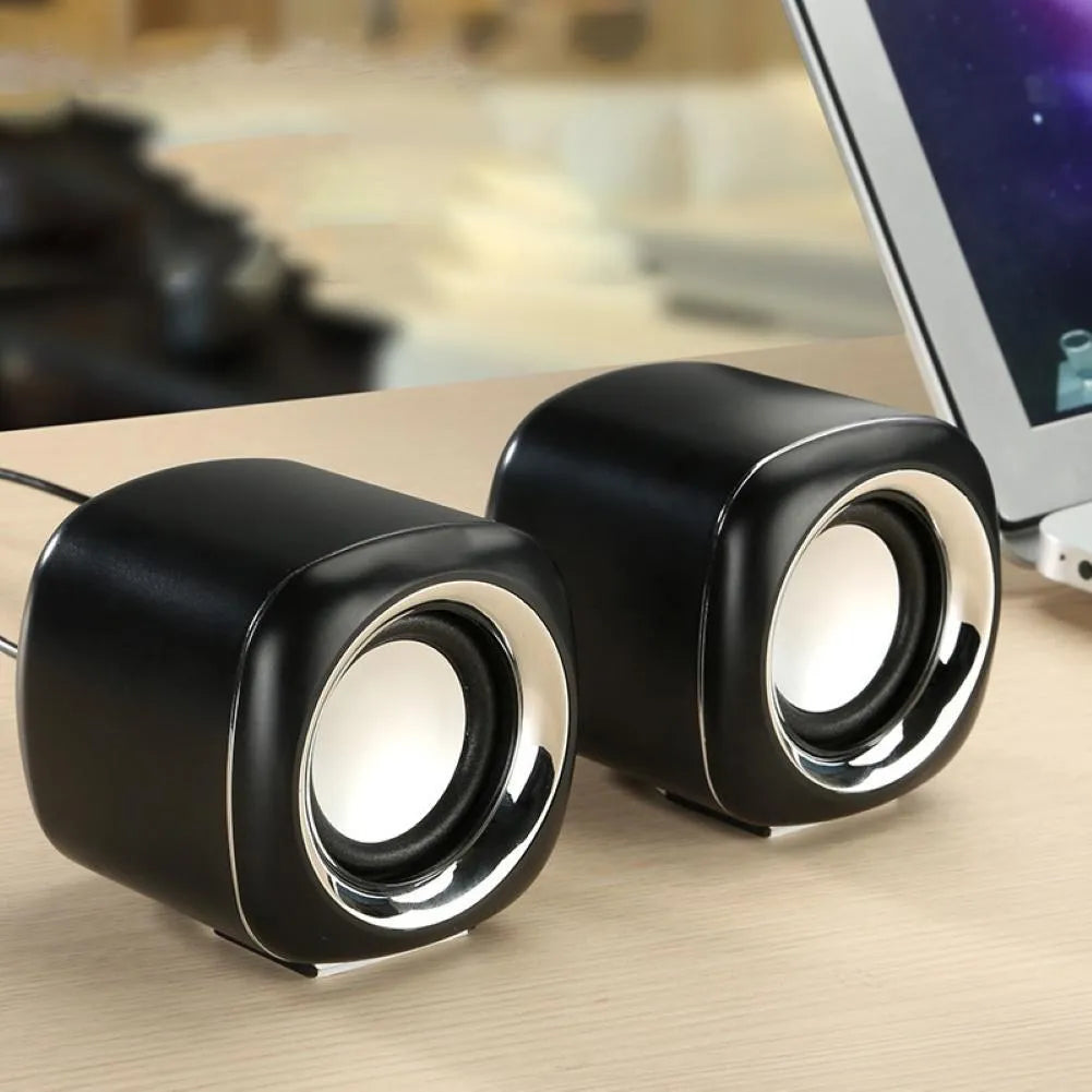 Pair of small black cube-shaped wired computer speakers with a 3.5mm plug on a desk