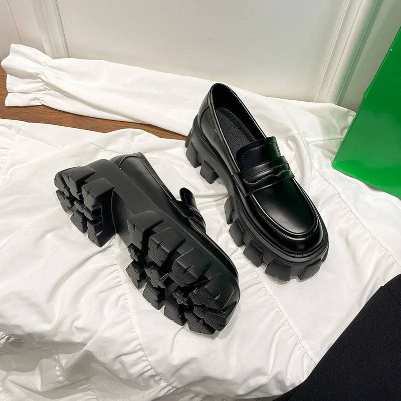 A pair of wide fit patent leather loafers with a rubber sole and muffin heel base.