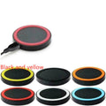 Square wireless charging base for mobile phones in six colour options on a wooden desk.