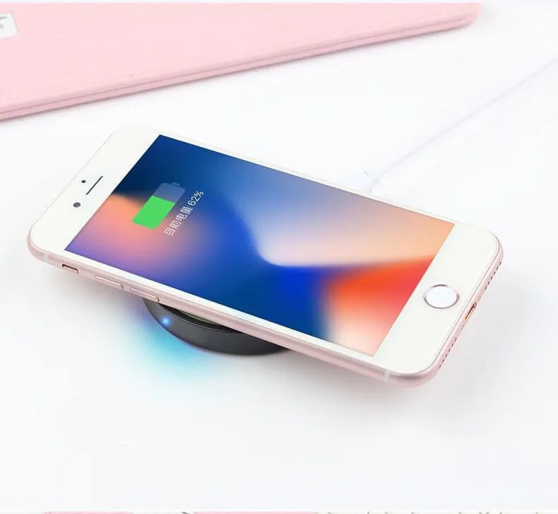 Square wireless charging base for mobile phones in six colour options on a wooden desk.