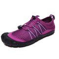 Unisex black quick-dry water shoes with mesh upper and elastic band, shown on a rocky riverbank.