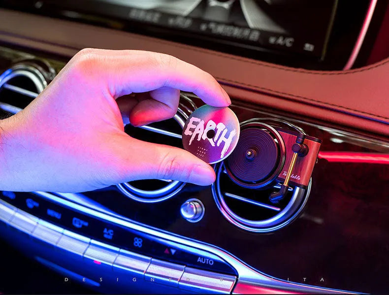 Brown alloy solid car perfume with record locomotive design clipped to a car air vent.