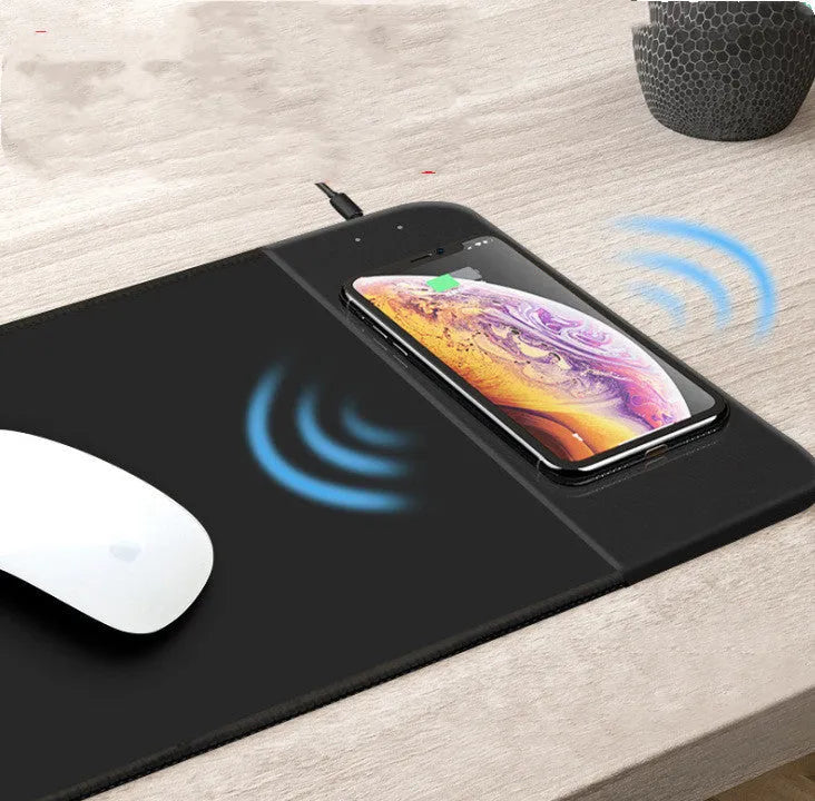 Black wireless charging mouse pad with RGB lighting on a desk, showing cloth surface and rubber base.