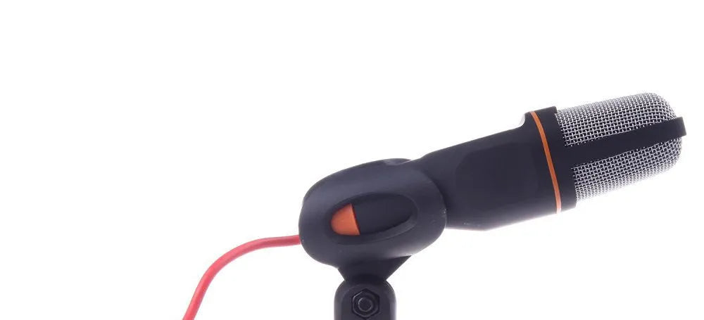 Black wired PC microphone with a clip holder on a desk next to a computer.