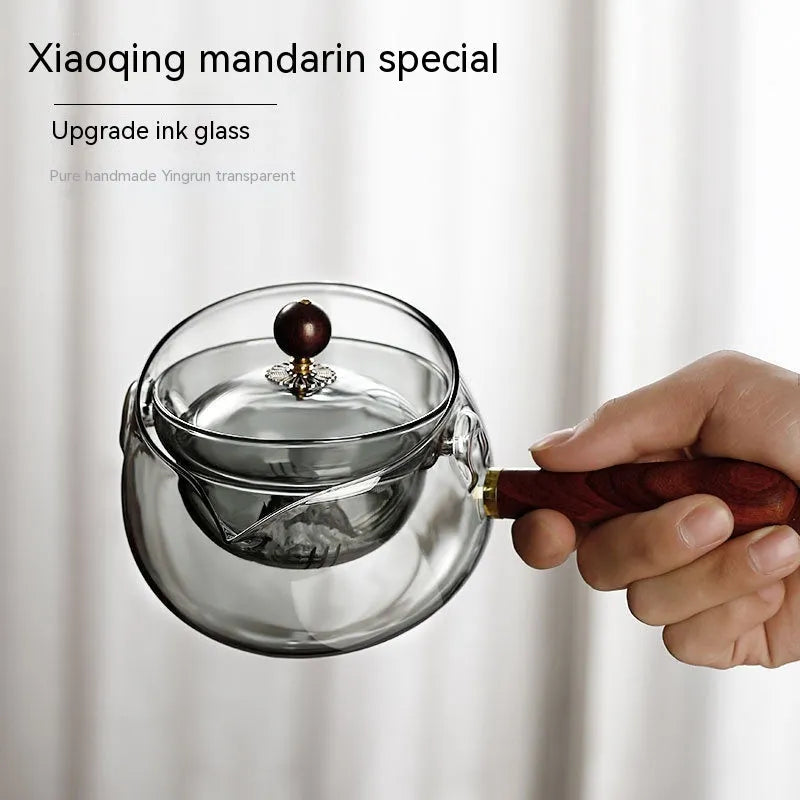 Semi-automatic rotary heat-resistant glass teapot with infuser and wooden handle on a table, transparent or grey