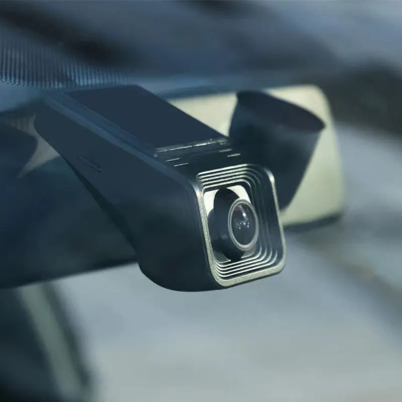 Black car dash cam mounted on windscreen with forward-facing lens and power cable