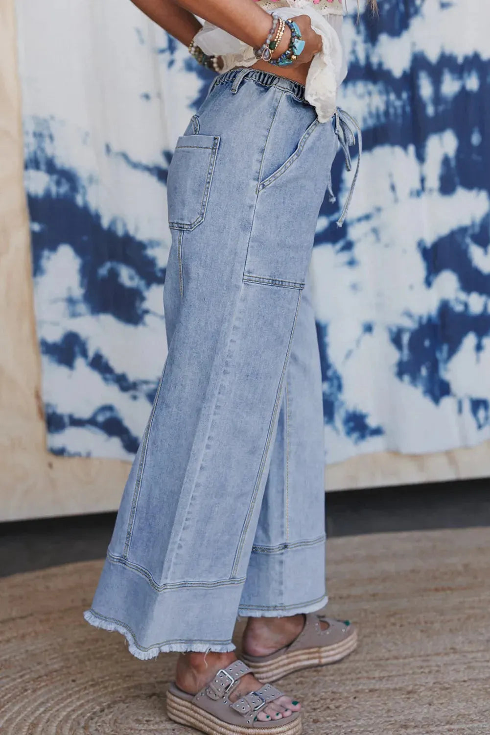 Beau blue women's wide leg denim trousers with a drawstring waistband and raw hem detail laid flat.