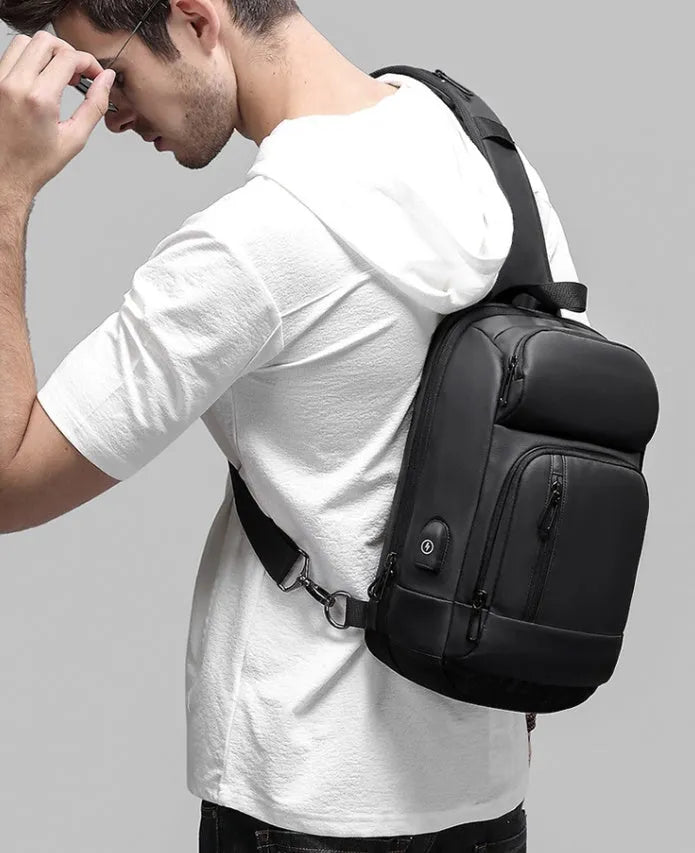 Black PVC outdoor shoulder bag with a square shape, showing the air cushion strap and front pocket.