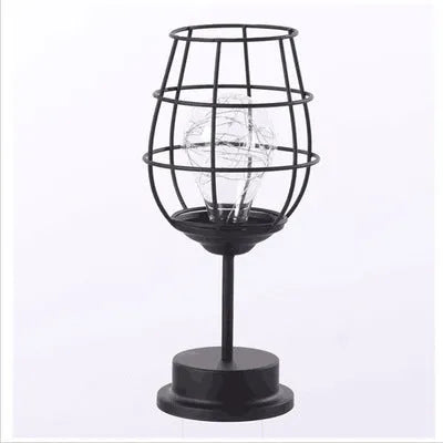 Minimalist hollow wrought iron table lamp in red wine bottle style on a wooden desk.