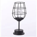 Minimalist hollow wrought iron table lamp in red wine bottle style on a wooden desk.