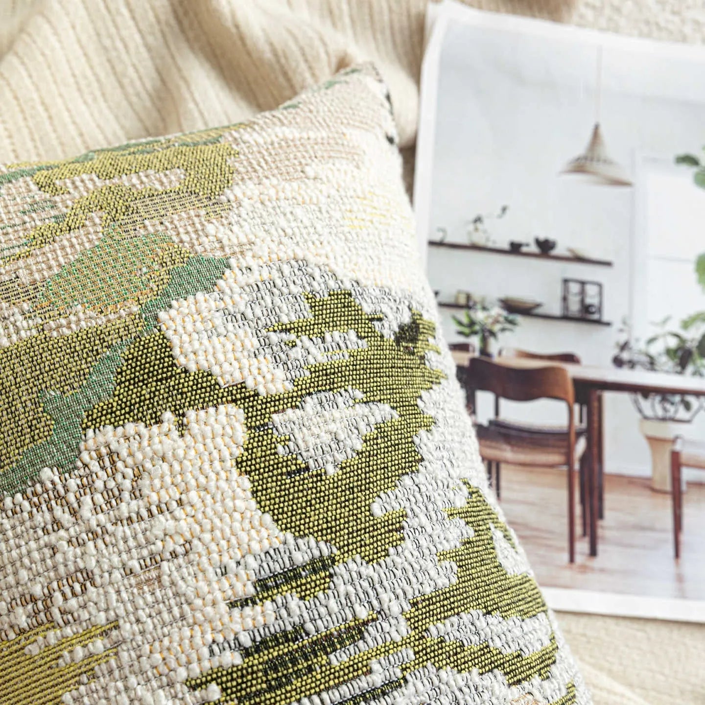 Green square pillow with abstract botanical plant and flower pattern on a sofa.