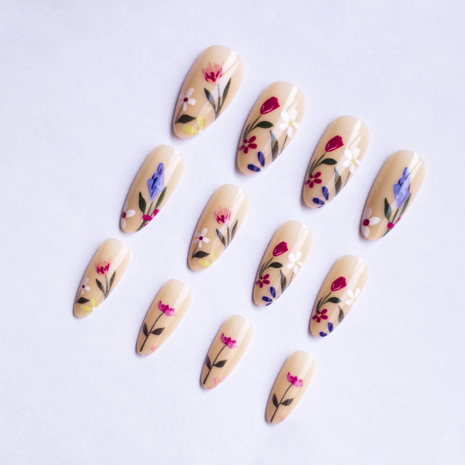Almond-shaped removable false nails with rose and tulip floral designs on a solid colour background.