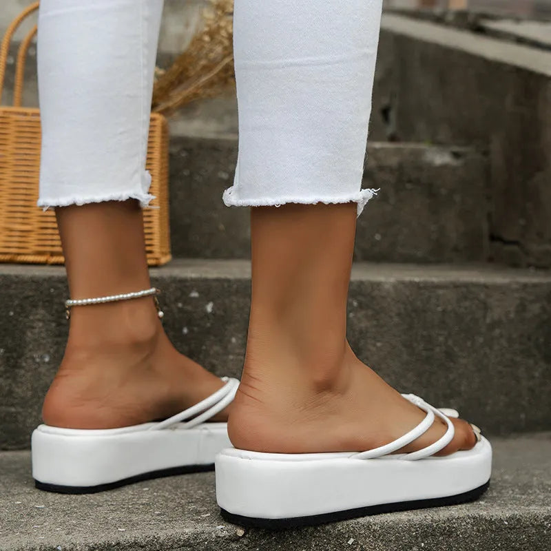 Women's white thick-sole flip-flops with round toe and herringbone patterned rubber sole on sand.