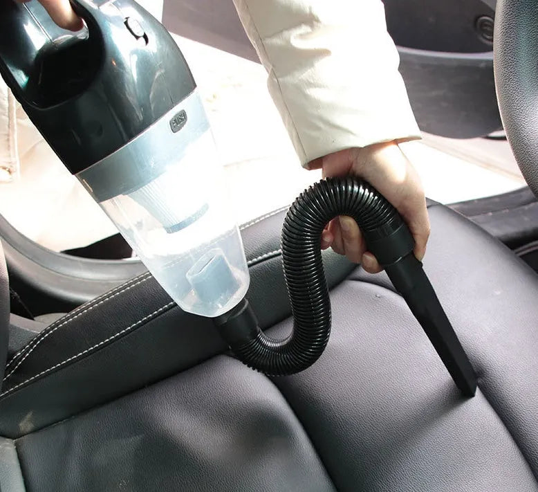 Orange handheld 12v car vacuum cleaner with nozzle attached on a car seat.