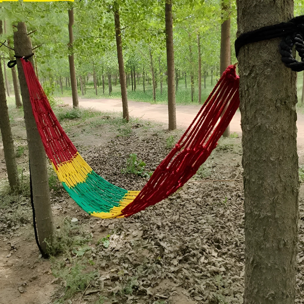 Outdoor nylon rope mesh hammock hung between two trees showing its open weave and supplied tying hardware.