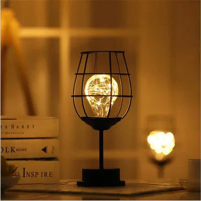 Minimalist hollow wrought iron table lamp in red wine bottle style on a wooden desk.