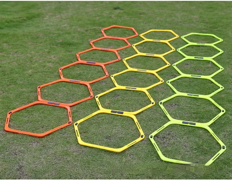 Six foldable hexagon agility training rings in green, orange, and yellow colours laid out on grass.