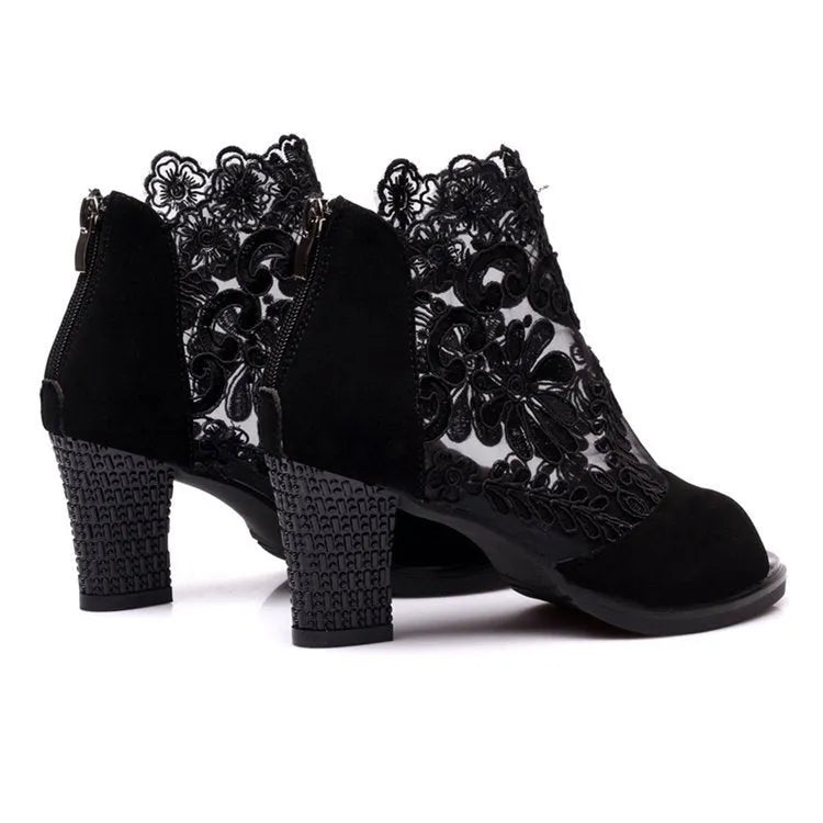 Black lace gladiator sandals with a square high heel and zip closure on a woman's foot.