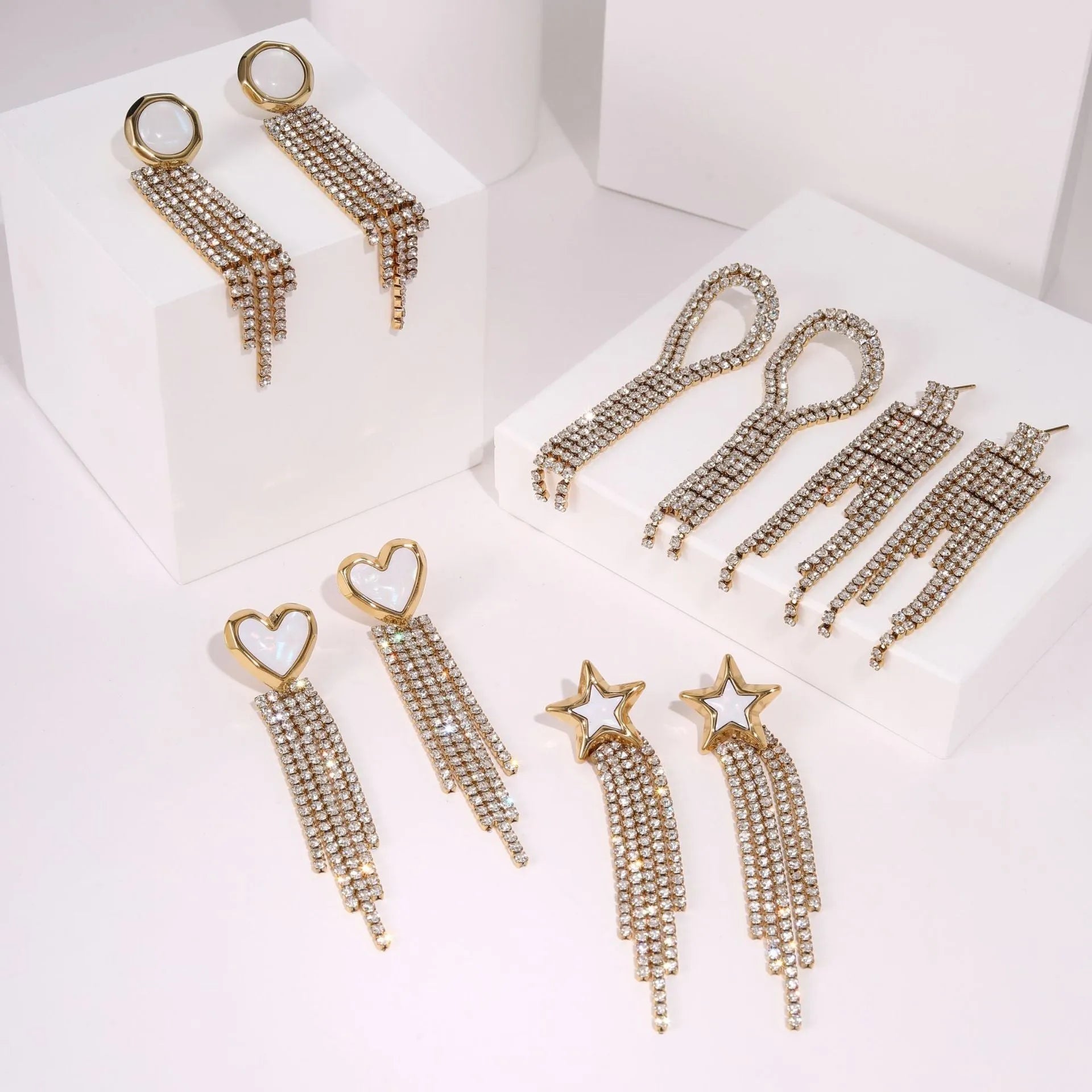 Gold-coloured stainless steel earrings with geometric heart, star, and tassel designs on a white background.