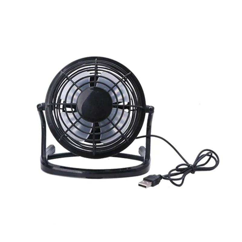 Mini black USB desk fan on a table next to a laptop, showing adjustable tilt angle.