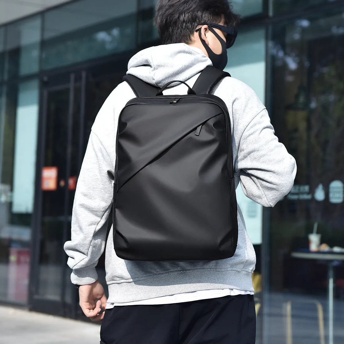 Men's waterproof PU backpack in black with simple sewing thread design and separate computer compartment.