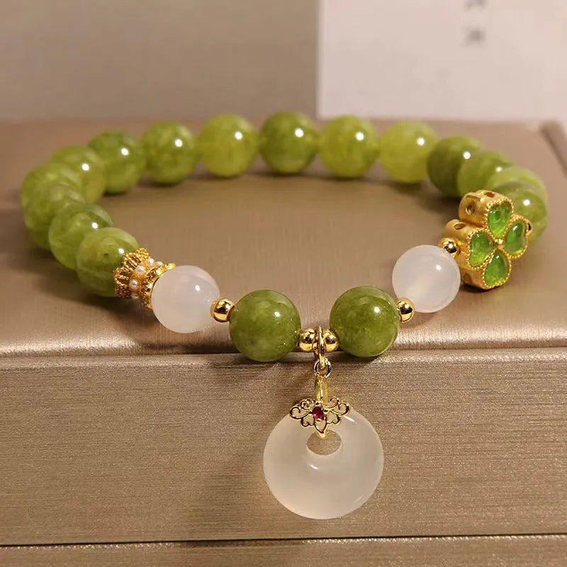 Women's green tourmaline bracelet with four-leaf clover charm and geometric drop pendant on a safety buckle.