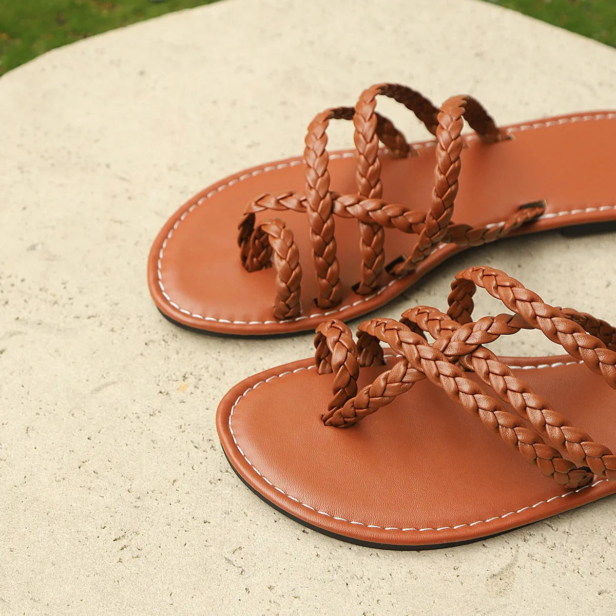 Womens woven clip-toe Roman sandals in black, brown, or white with a flat rubber sole.
