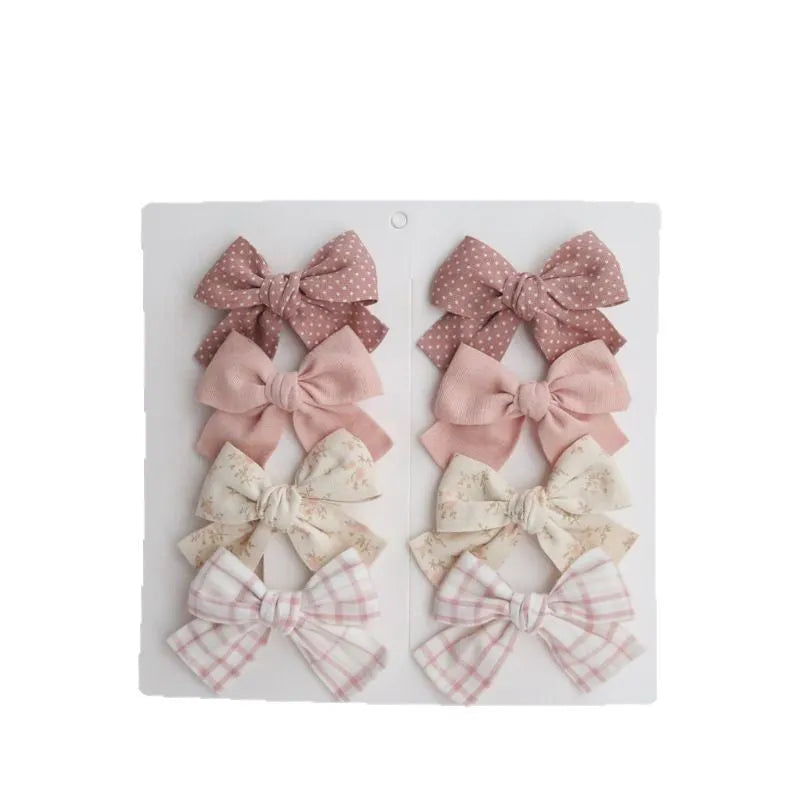 Set of eight cloth hairclips for children with dovetail bow designs in various colour patterns.