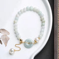 Green jade peace buckle charm and pearl beaded bracelet for women on a white background.