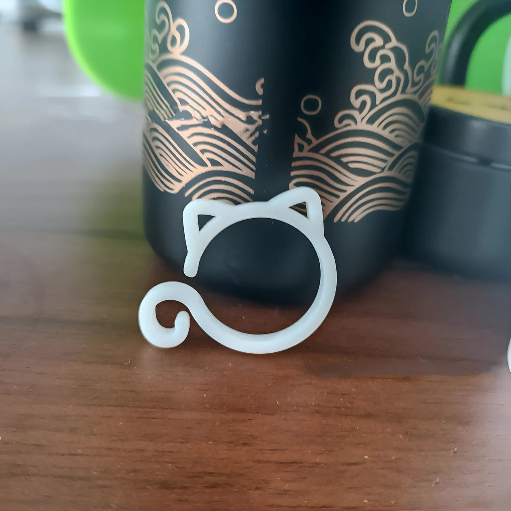 Small red cat-shaped plastic plant clip on a green leaf stem