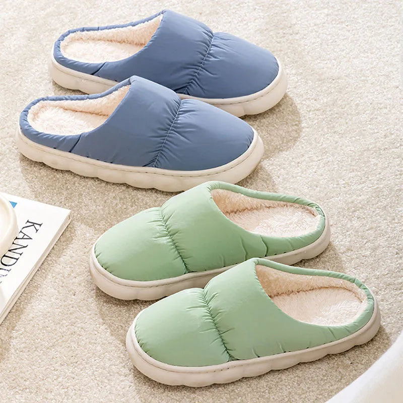 A pair of blue down cotton slippers with a thick rubber sole and artificial leather upper on a wooden floor.