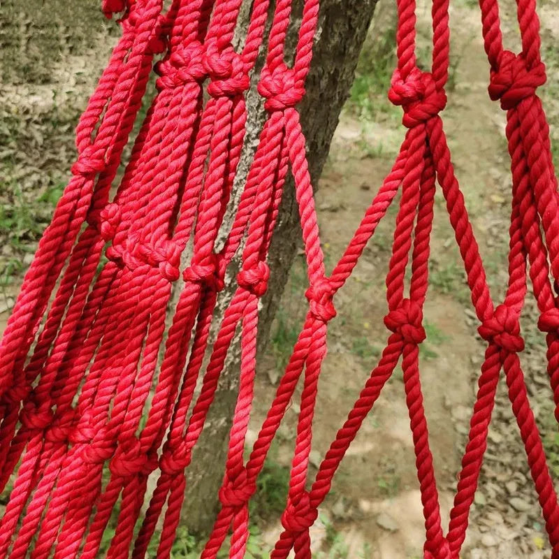 Outdoor nylon rope mesh hammock hung between two trees showing its open weave and supplied tying hardware.