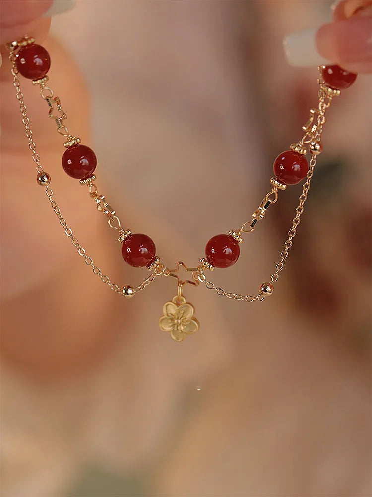Close-up of a red agate double layer bracelet with floral and peach blossom detailing on a woman's wrist.