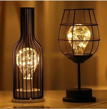 Minimalist hollow wrought iron table lamp in red wine bottle style on a wooden desk.